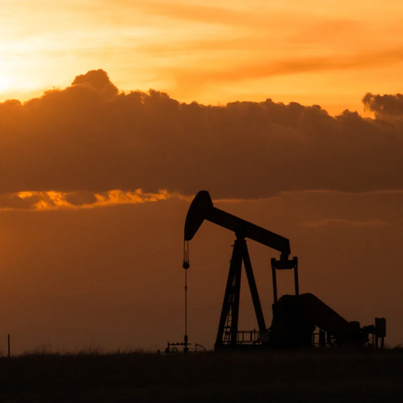 Pumpjack silhouetted against an orange sunset sky